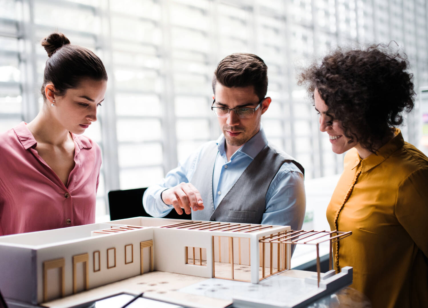 Group of young architects with model of a house standing in office, talking.